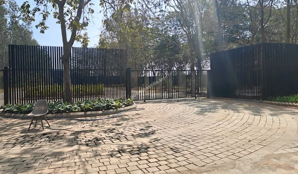 A close-up view of the Godrej Castillo gated entryway showing the tall black metal fencing and an existing tree preserved within a circular planter.