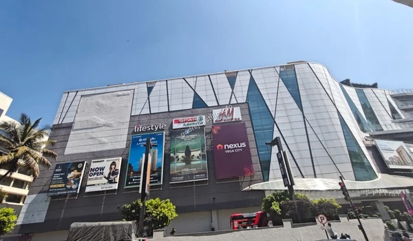 Large exterior facade of Nexus Vega City mall featuring major anchor stores like Lifestyle, Spar, and H&M, located a short distance from Godrej Castillo.