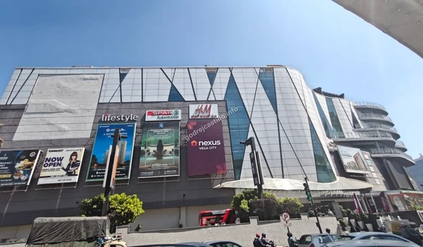 Street-level perspective of the sprawling Nexus Vega City shopping center showcasing multiple brand billboards near the Godrej Castillo project.