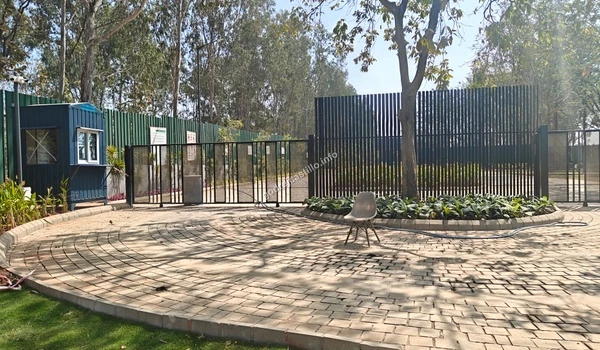 View of the security checkpoint at Godrej Castillo featuring a blue guard cabin, a black metal fence, and a beautifully patterned paved driveway.