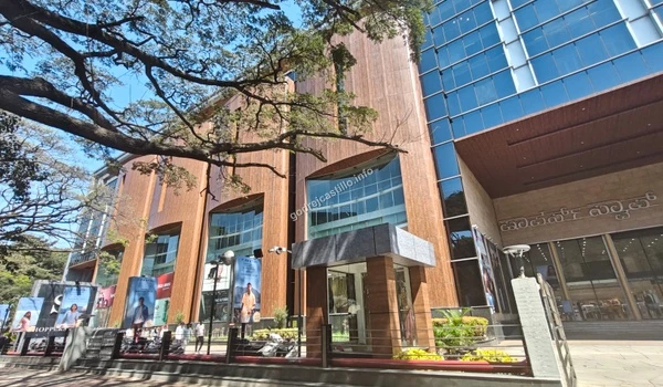 Expansive outdoor view showcasing the wooden and glass exterior of the Shoppers Stop retail mall under large shade trees near Godrej Castillo